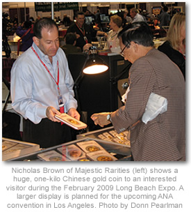 Nicholas Brown of Majestic Rarities (left) shows a huge, one-kilo Chinese gold coin to an interested visitor during the February 2009 Long Beach Expo. A larger display is planned for the upcoming ANA convention in Los Angeles. Photo by Donn Pearlman